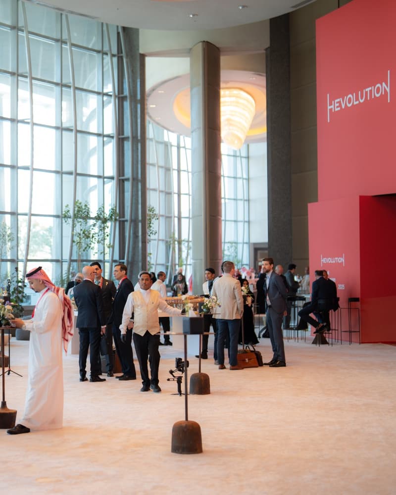 Riyadh summit event environment with Hevolution branding, attendees, event-floor activity, tall glass windows, and large venue signage.